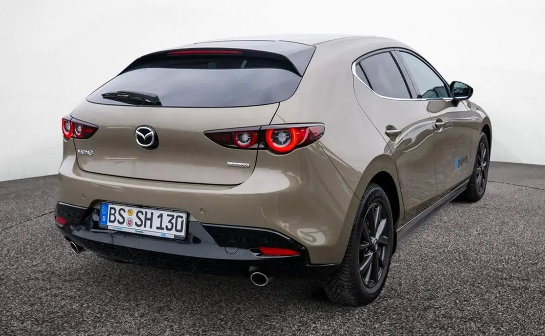 Heck eines Mazda 3 in der Farbe platinum-quartz, der auf dem Hof des Autohauses Hempel in Braunschweig steht.